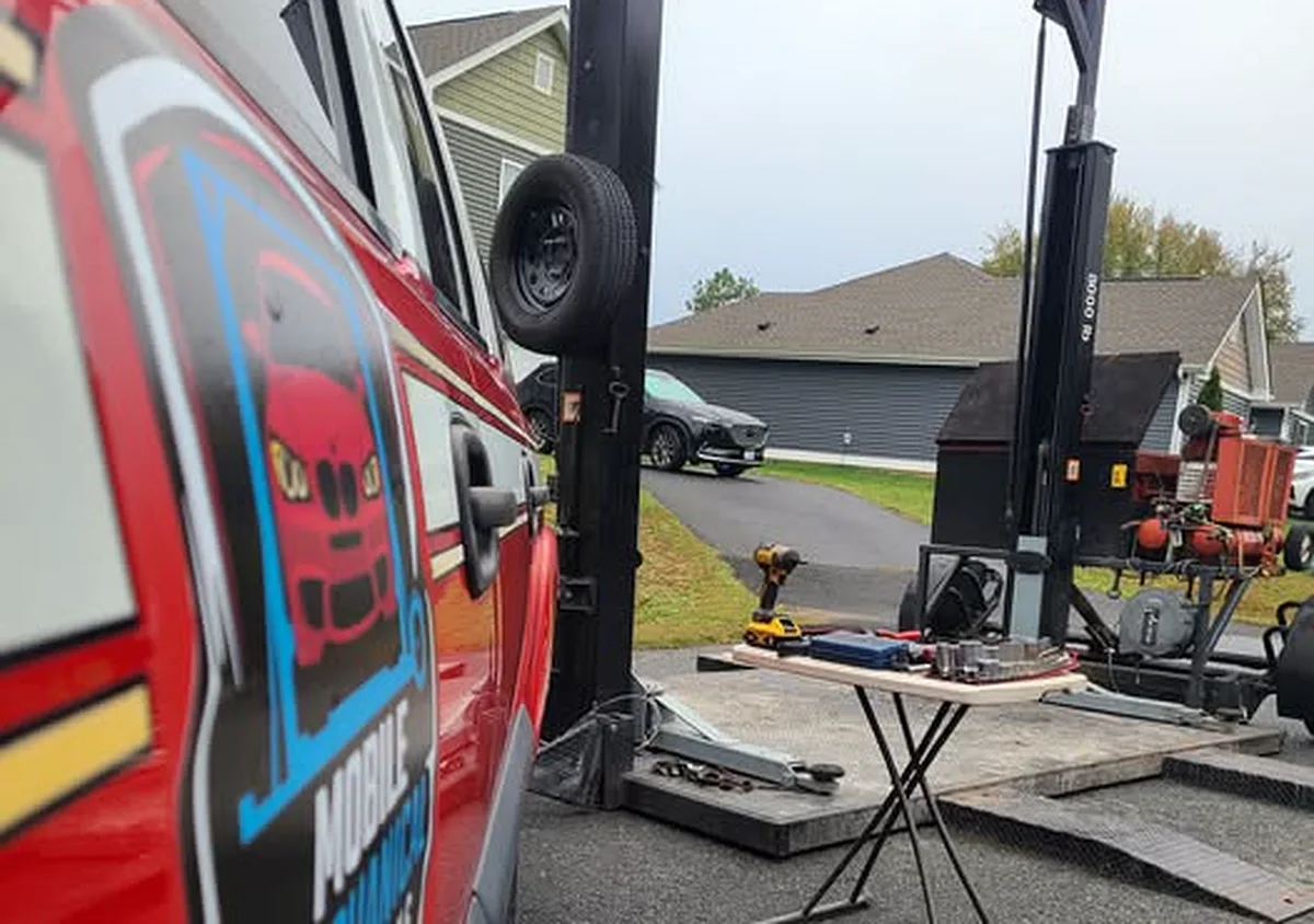 Portable two-post lift set up in a driveway next to the Mobile Mechanical Solutions truck